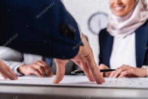 cropped view of smiling arabian woman near blueprint and multicultural businessmen, blurred background